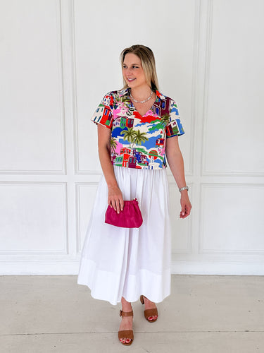 Woman wearing a colorful patterned shirt and white skirt with a pink clutch against a white background