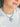 A close-up of a person wearing a light blue heart-shaped pendant necklace with a twisted light blue and white cord, paired with a white ribbed top.