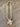 A statement necklace featuring a textured beige woven mesh collar and a central flower-shaped pendant with a white faux pearl surrounded by clear rhinestones, displayed on a wooden surface.