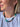 A close-up of a woman wearing a multi-colored beaded necklace made of green, brown, black, and white beads, paired with a white t-shirt and a small silver stud earring.