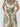 A sleeveless collared dress with a ruffled V-neckline and a matching waist tie, featuring an ornate baroque-style pattern in green, gold, and brown on an off-white background. The model is standing against a white brick wall.