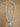 A light blue twisted rope necklace with a heart-shaped light blue stone pendant, displayed on a brown wooden surface.