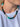 A close-up of a person wearing a beaded necklace made of alternating sections of turquoise, dark green, black, cream, and brown polished beads, paired with a white t-shirt.