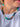 A close-up of a person wearing a multi-colored beaded necklace made of disc-shaped beads in teal, green, brown, cream, and black, paired with a white t-shirt.