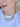 A close-up of a woman wearing a gold-toned statement necklace with three coin-style medallions and small clear stones, paired with a white top.