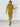A woman modeling a short-sleeve Chartreuse  midi dress with a button-down front, standing against a white brick wall.
