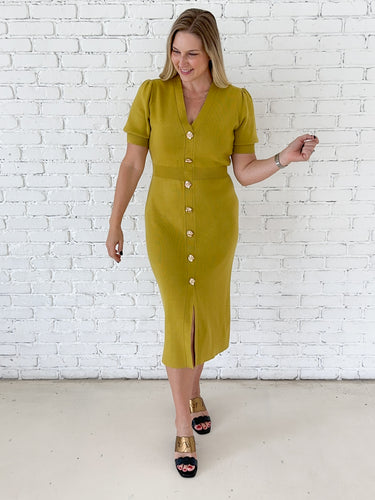 A woman modeling a short-sleeve Chartreuse  midi dress with a button-down front, standing against a white brick wall.