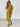 A woman modeling a short-sleeve Chartreuse midi dress with a button-down front, standing against a white brick wall.